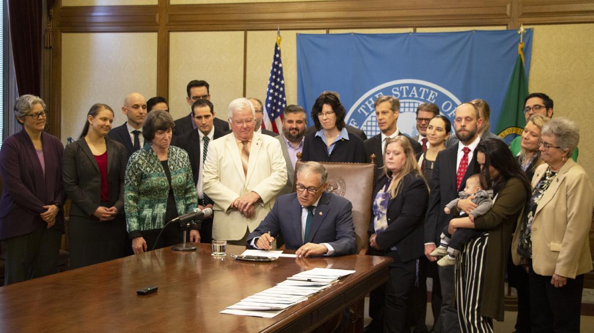 Governor Inslee signs Senate Bill 5297 as a group of Assistant Attorneys General watches